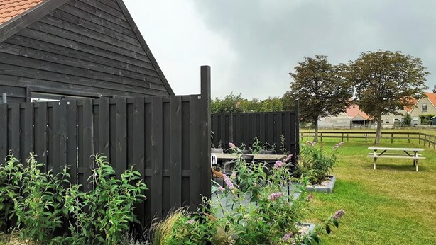 A wooden structure with a sloped roof, surrounded by a grassy area with a picnic table and a bench.