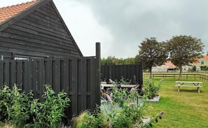 Eine Holzhütte mit geneigtem Dach, umgeben von einer Rasenfläche mit Picknicktisch und Bank.
