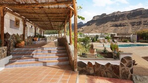 A covered outdoor area with steps leading to a pool, surrounded by stone walls and potted plants. - Pet-Friendly 'Finca Rural Los Tanquillos' with Mountain View, Pool, Wi-Fi, A/C, Terrace & Garden (San Bartolomé de Tirajana)