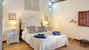 A bedroom with a bed, two bedside tables, a nightstand, a wall-mounted coat rack, and a wooden bench. - Pet-Friendly 'Finca Rural Los Tanquillos' with Mountain View, Pool, Wi-Fi, A/C, Terrace & Garden (San Bartolomé de Tirajana)