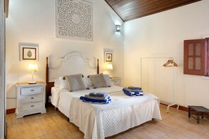 Une chambre à coucher comprenant un lit, deux tables de chevet, une commode, un porte-manteau mural et un banc en bois.