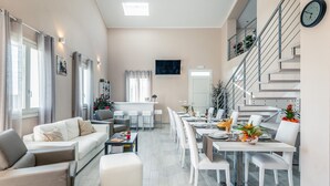 A modern living room with a sofa, a coffee table, and a dining area with chairs and a table set for a meal. - Villa Le Terme with Pool, Whirlpool, Garden, Terrace, BBQ, A/C & Wi-Fi (Monsummano Terme PT)