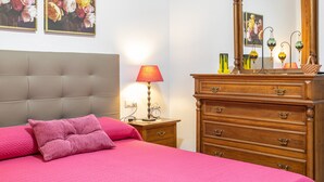 Et soveværelse med seng, kommode, natbord, lampe og spejl.