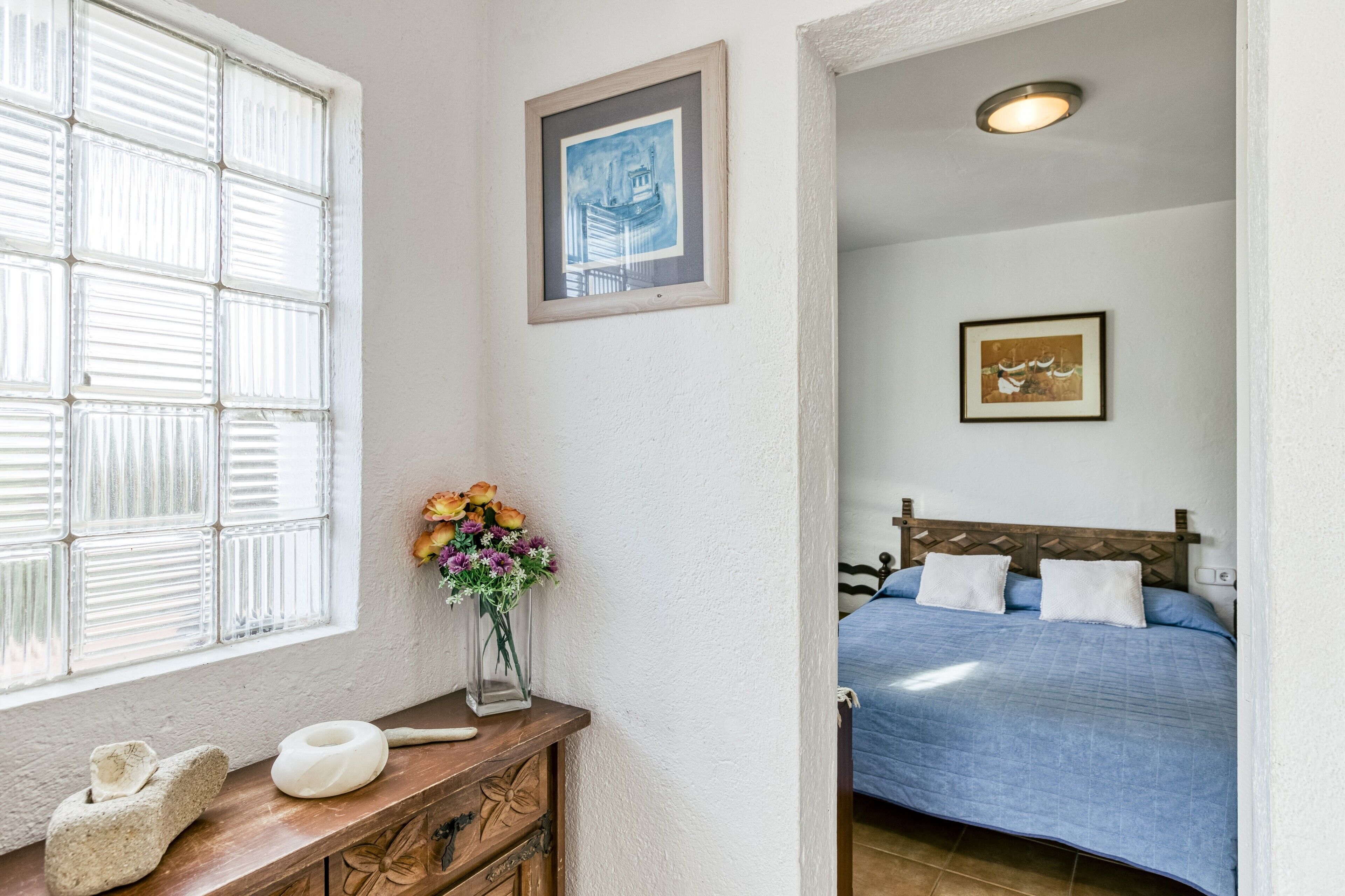 A bedroom with a bed, a nightstand, a window with blinds, and a framed picture on the wall.