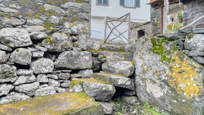 A stone wall with a wooden structure, a building with a balcony, and a mountain backdrop. - Casa Familia Pestana 1, a Home in Madeira (Seixal)
