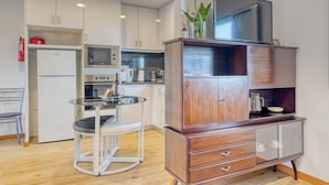 Una cocina moderna con armarios blancos, horno empotrado, microondas y un pequeño comedor con una mesa de vidrio y dos sillas.