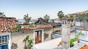 Una terraza en la azotea con techo de tejas, un pilar de piedra y vistas al mar.