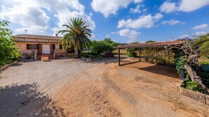 Una propietat rural amb una entrada de carrer de terra, una zona d'estar coberta a l'aire lliure i una casa amb teulada de rajola.