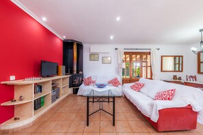 A living room with a red wall, a sofa, a television, a fireplace, and a dining table.