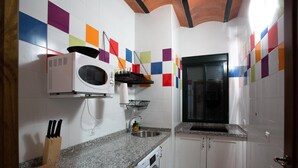 A kitchen with white cabinets, a granite countertop, a microwave, a washing machine, and a sink.