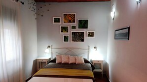 A bedroom with a bed, two bedside tables, a nightstand, a dresser, and a wall with several framed pictures.