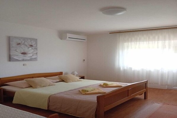 A bedroom with a bed, a nightstand, an air conditioner, and a window with curtains.