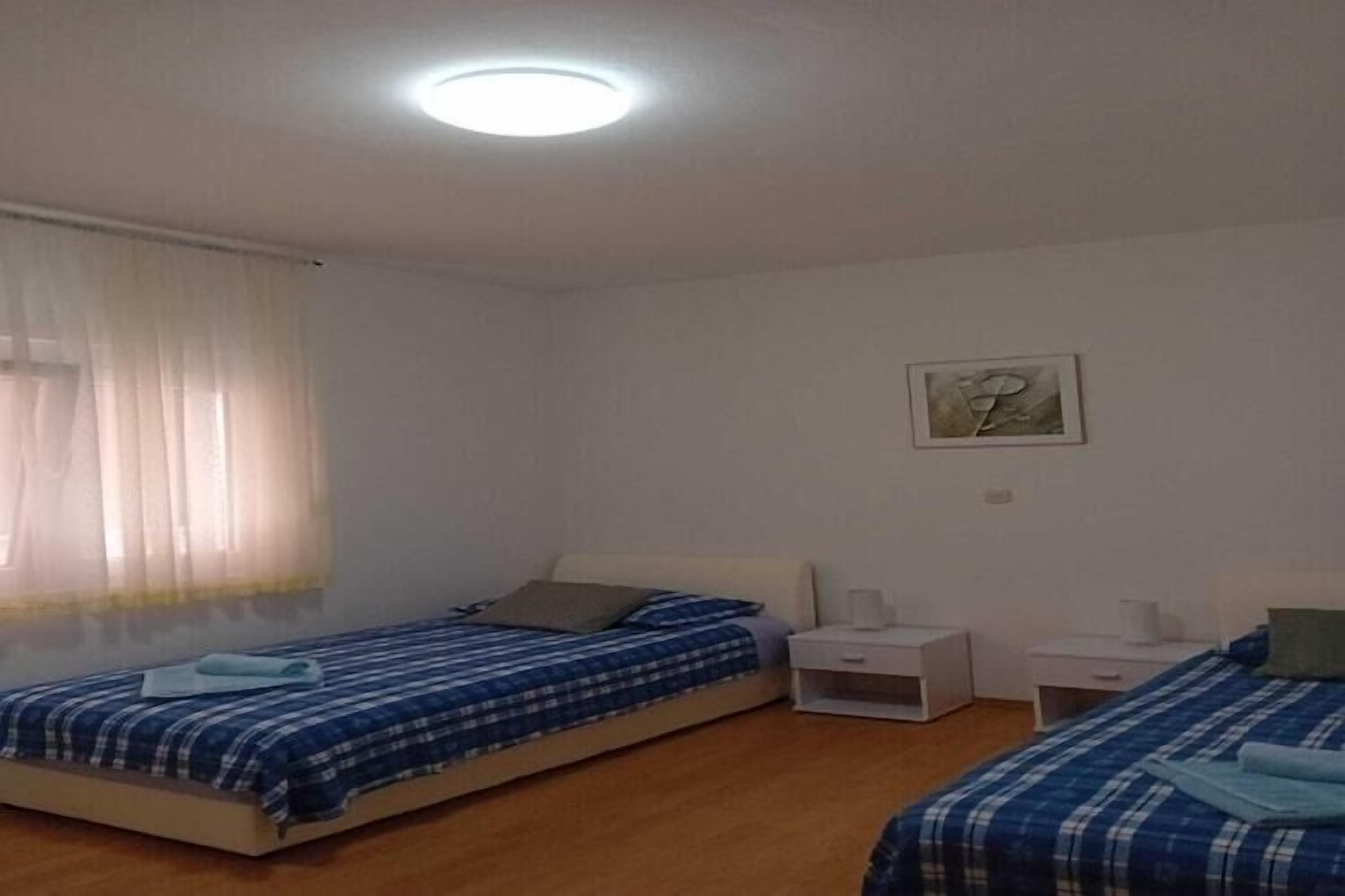 A bedroom with two beds, a ceiling light, a window with curtains, and a wall-mounted picture.