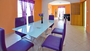 Un área de comedor con una mesa de vidrio y sillas moradas, paredes anaranjadas y una puerta de madera.