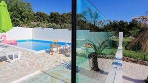 Zona de piscina con suelo de piedra, un flotador de flamenco rosa y una mesa con dos botellas amarillas.