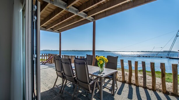 A covered outdoor seating area with a table and chairs, overlooking a body of water with a bridge in the background. - Apartment in Zeeland with Private Jetty (Kamperland)