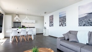 A modern living room with a grey sofa, a wooden coffee table, and a dining area with white chairs and a kitchen in the background. - Apartment in Zeeland with Private Jetty (Kamperland)