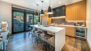A modern kitchen with a large island, bar stools, pendant lighting, and a view through large sliding doors. - One Snowmass West 503 (Snowmass)