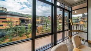 A modern hotel room with large windows offering a view of the surrounding buildings and greenery. - One Snowmass West 503 (Snowmass)