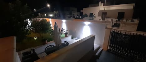 A rooftop terrace with a white railing, potted plants, and a statue.