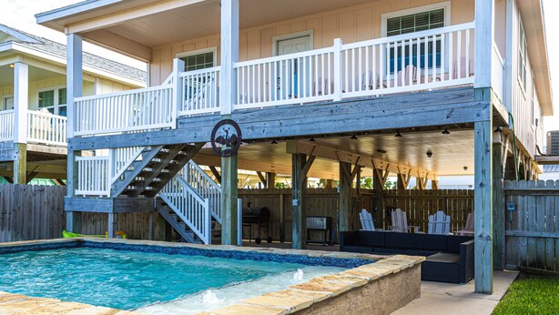 A two-story house with a covered patio, a pool, and a barbecue area.