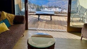 Ein modernes Wohnzimmer mit einer Couch, einem runden Couchtisch und Blick auf schneebedeckte Berge durch große Schiebetüren.