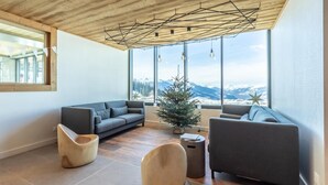 Ein modernes Wohnzimmer mit Holzboden, großen Fenstern mit Bergblick, einem kleinen Weihnachtsbaum und zwei Sofas.