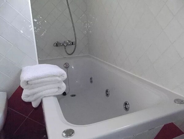 Une salle de bain avec une baignoire blanche, une pile de serviettes blanches et une pomme de douche.