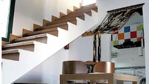Un intérieur moderne avec un escalier en bois, un coin repas et une cuisine visible à travers une porte ouverte.