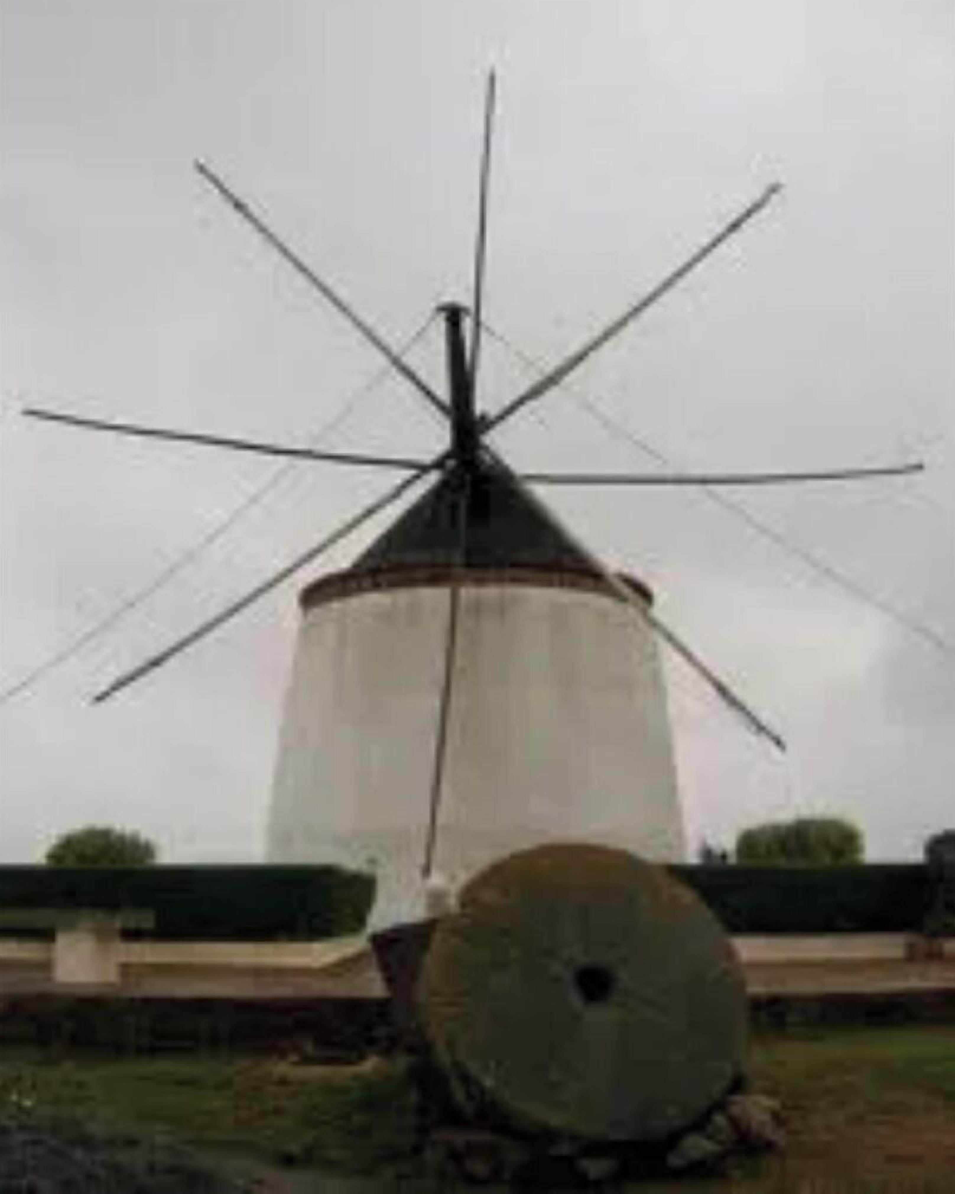 Un molino con una vela grande y una base cilíndrica, rodeado de un área cubierta de césped.