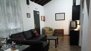 Un salon comprenant un canapé, un fauteuil, une table basse, un téléviseur et un petit meuble.