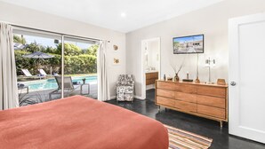 Een slaapkamer met een groot bed, een houten dressoir, een televisie en uitzicht op een zwembad.