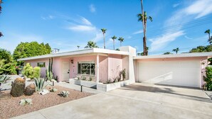 Een tweelaags huis met garage, een klein voortuintje en een aangelegde tuin met cactussen en andere woestijnplanten.