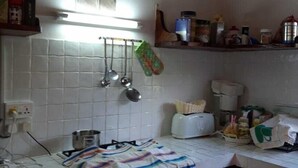 Ett kök med vita, kaklade väggar, en hängande hylla för kastruller, en brödrost och diverse köksredskap på bänkskivan.