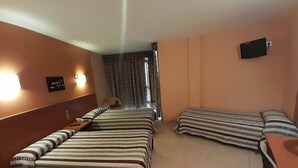A hotel room with two beds, a desk, a chair, a TV, and a window with patterned curtains. - HOTEL AVENIDA (El Morell)