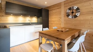 Een moderne keuken met een houten wandklok, witte stoelen en een houten eettafel.