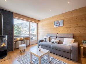 Un salon chaleureux avec une cheminée, un canapé, une table basse et une fenêtre donnant sur l’extérieur.