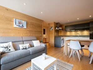 Un appartement moderne avec un canapé gris, une petite table à manger et un coin cuisine.