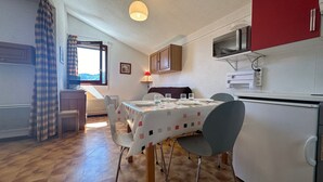 Una cocina compacta con zona de comedor, suelo de madera y ventana con cortinas.