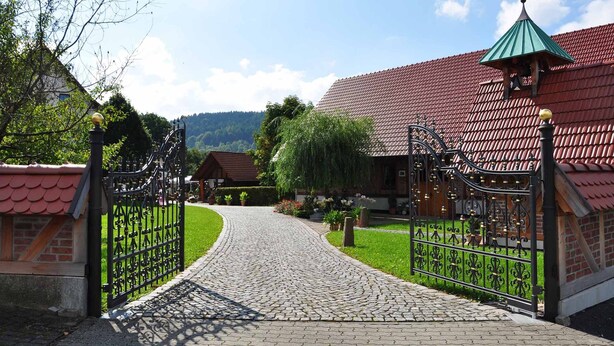 A cobblestone pathway leading to a gated entrance with a traditional metal gate and a bell tower. - Landhotel Zur Pferdetränke (Schleid)