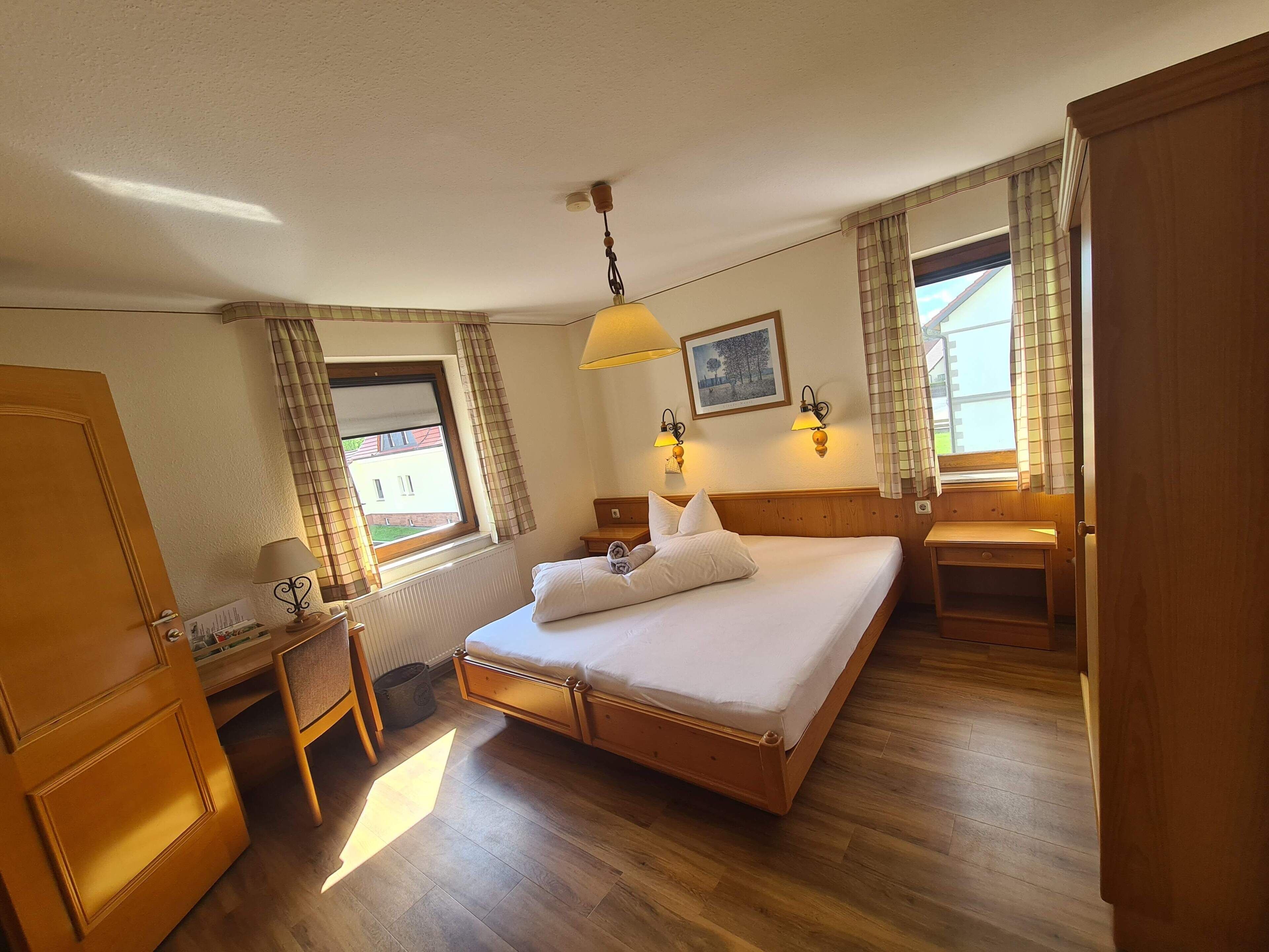 Una habitación de hotel con cama, mesita de noche, lámpara y ventana con cortinas.