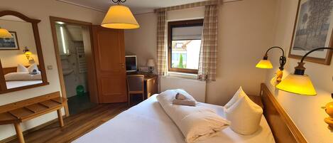 Habitación de hotel con cama, escritorio, silla y ventana con cortinas.