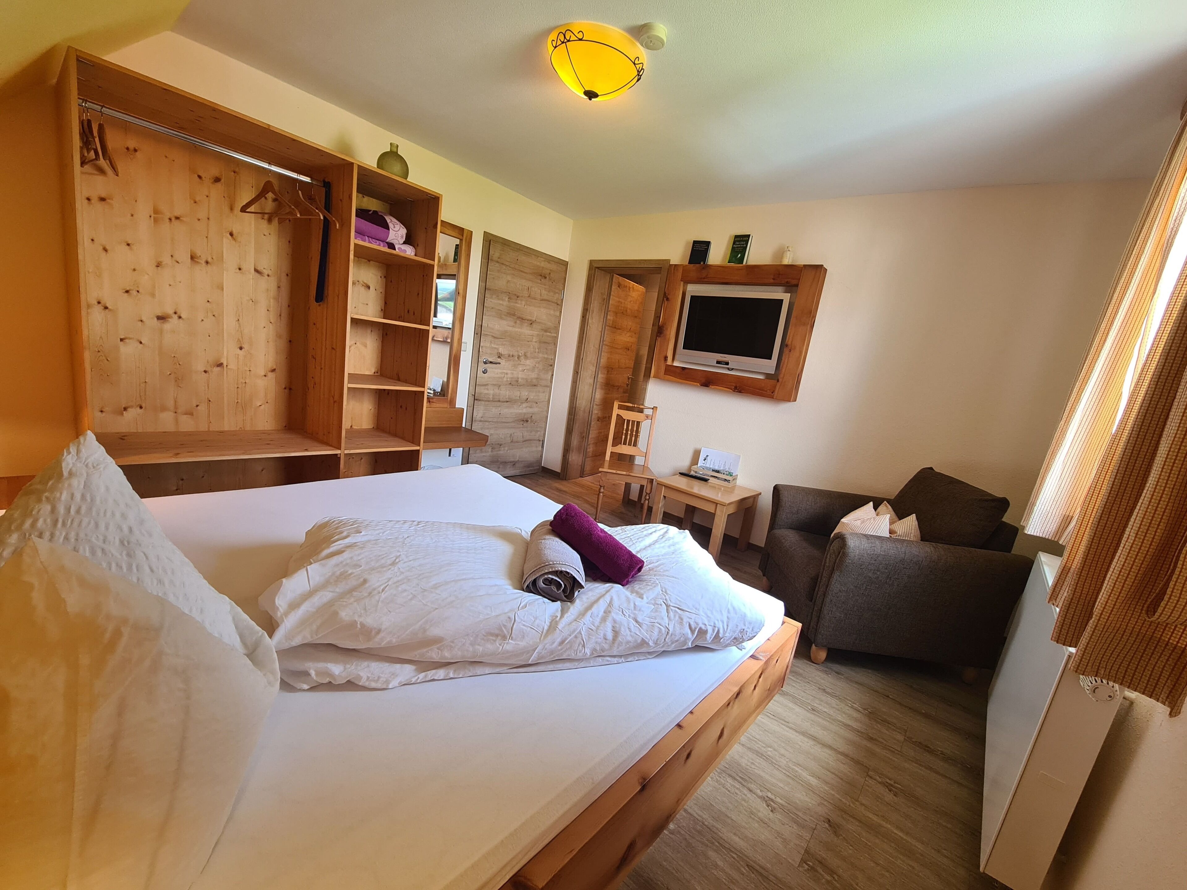 A bedroom with a bed, wooden wardrobe, TV, desk, and chair.