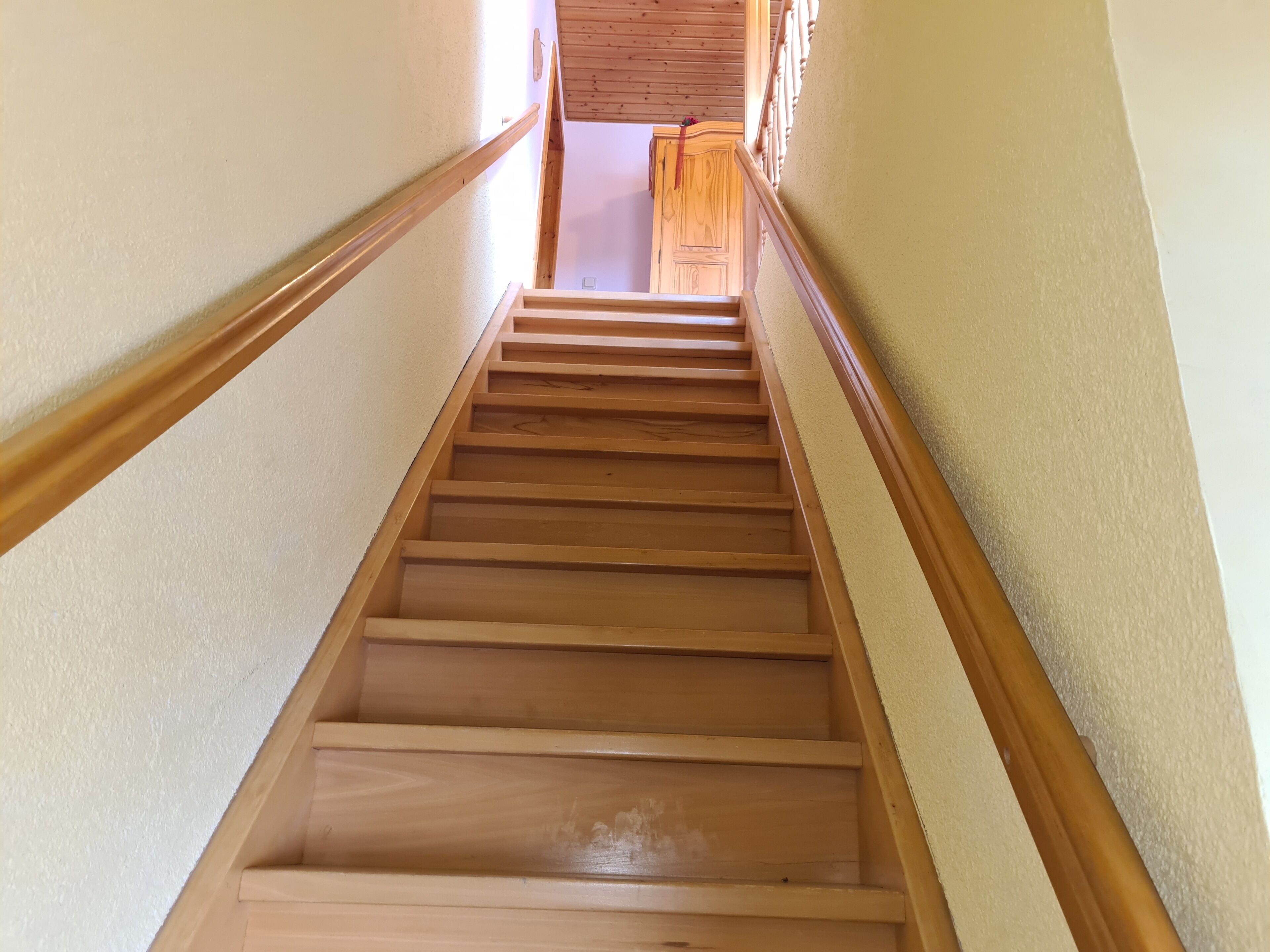 Eine Holztreppe mit Handlauf, die zu einem Raum mit einer Holztür und einem Fenster führt.