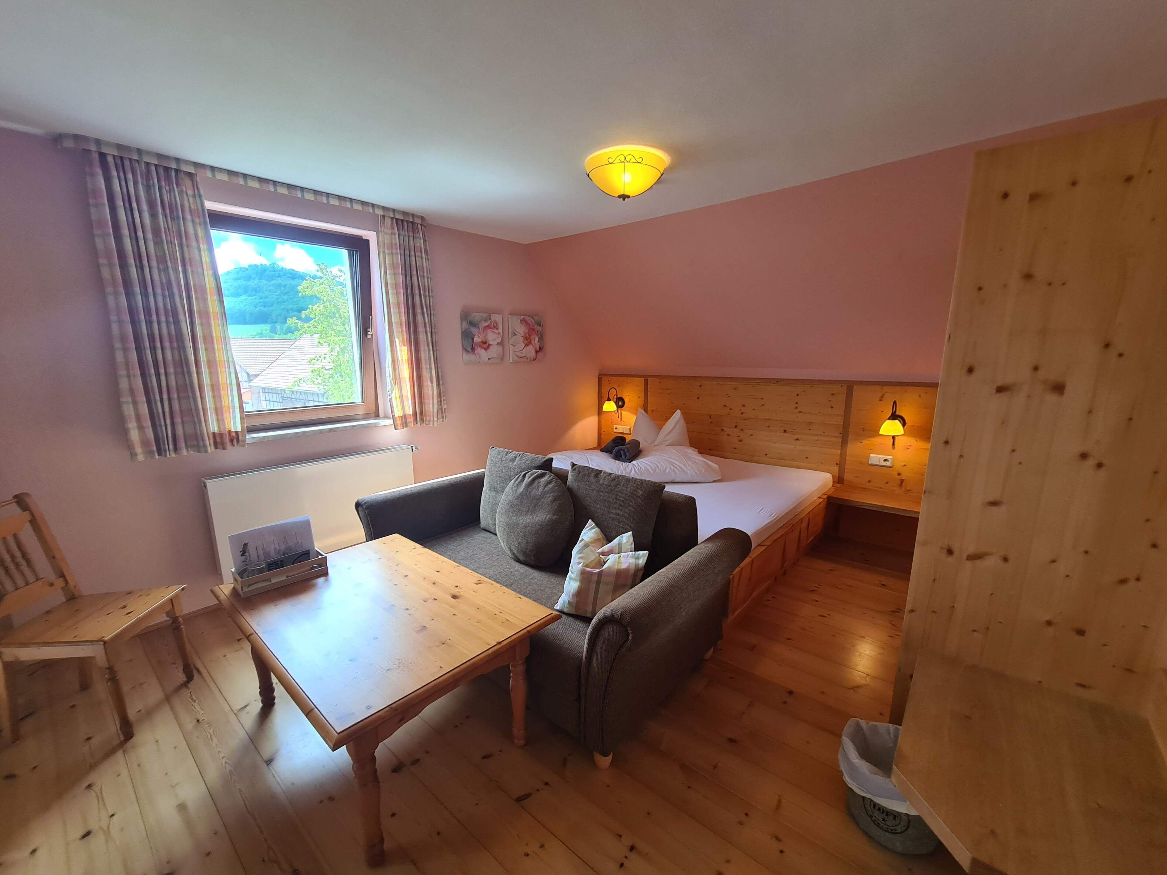 A room with a bed, a sofa, a table, a chair, and a window with curtains.