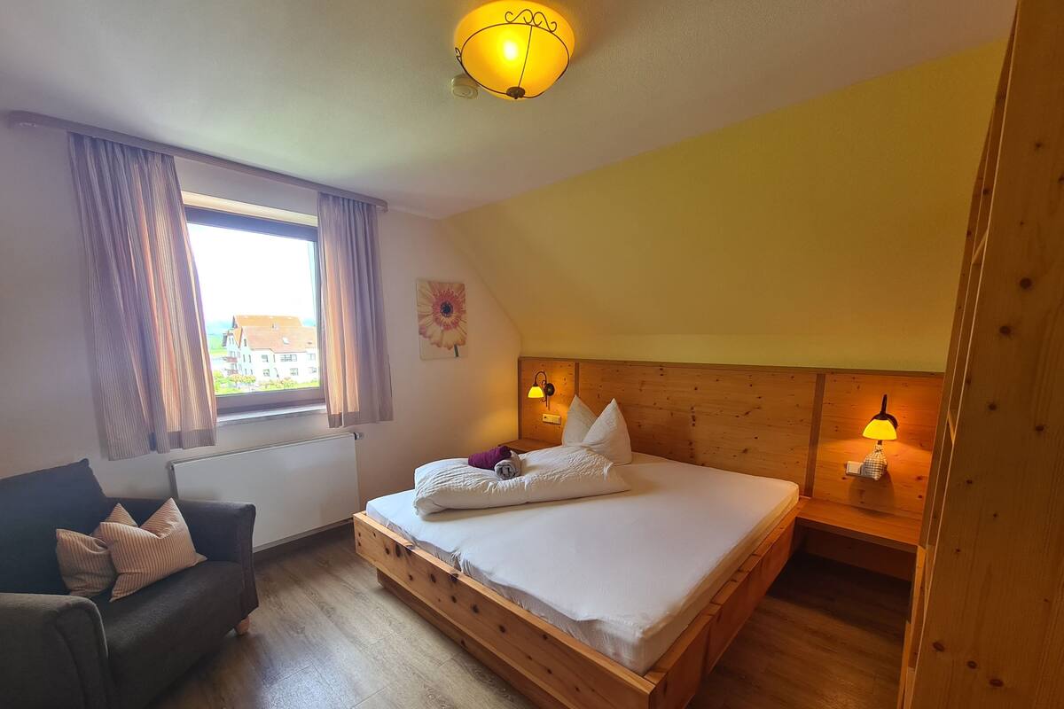 A bedroom with a wooden bed, two bedside lamps, a window with curtains, a wooden headboard, and a small table with a lamp.