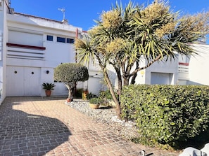 A paved driveway leading to a white building with a garage, a small tree, and a hedge. - Charming Holiday Home with Garden View, Terrace, Balcony & Parking in Royan (Royan)