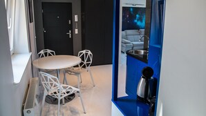 Une pièce moderne avec une table ronde et des chaises blanches, une porte noire et un mur d’accent bleu orné d’un miroir sur le thème de la galaxie.