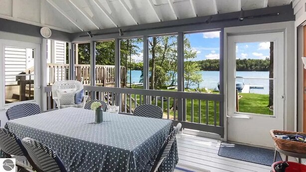En overdækket terrasse med et bord og stole, med udsigt over en sø.