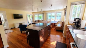 A modern kitchen with a central island, wooden flooring, and large windows offering a view of the outdoors.